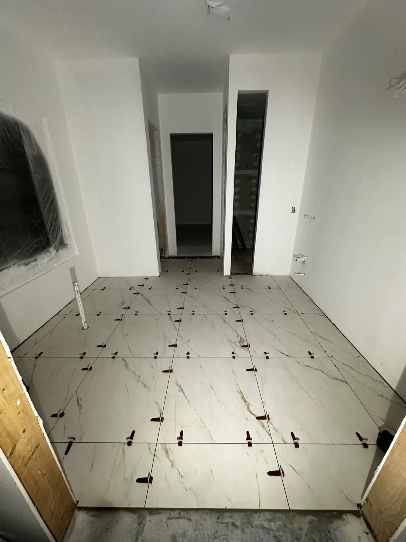 Piso de porcelanato grande tipo mármol recién colocado con niveladores en cada esquina
