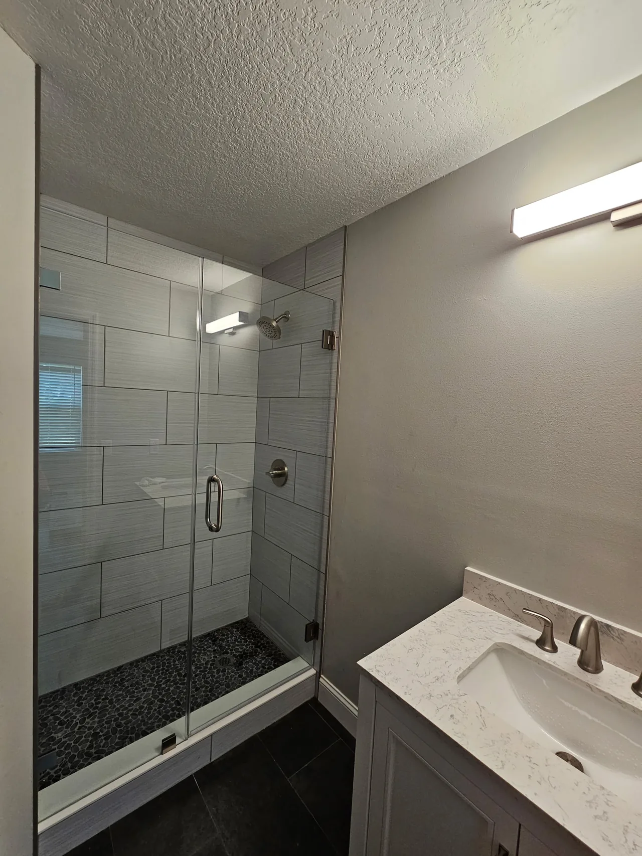 Ducha con porcelanato gris, piso de piedra de río y vidrio sin marco