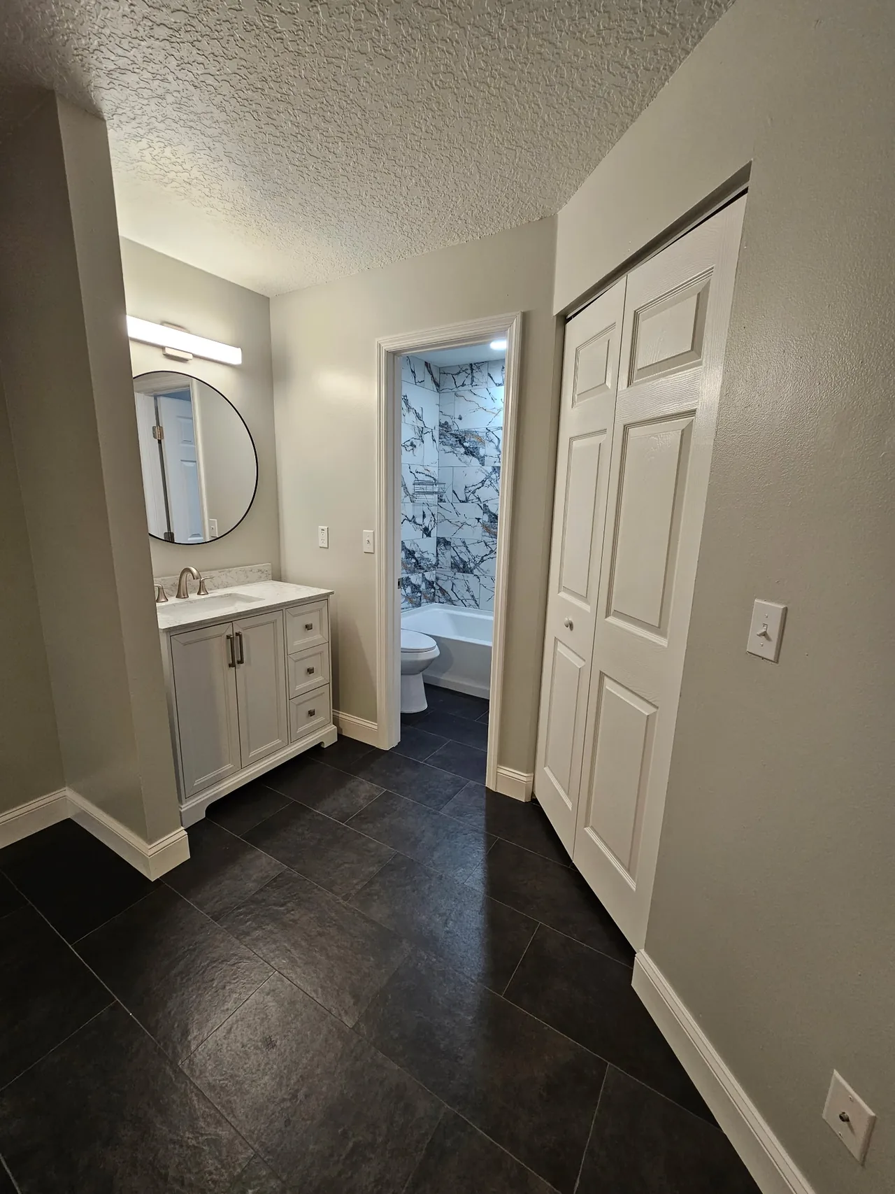 Un baño remodelado con tocador blanco y piso oscuro