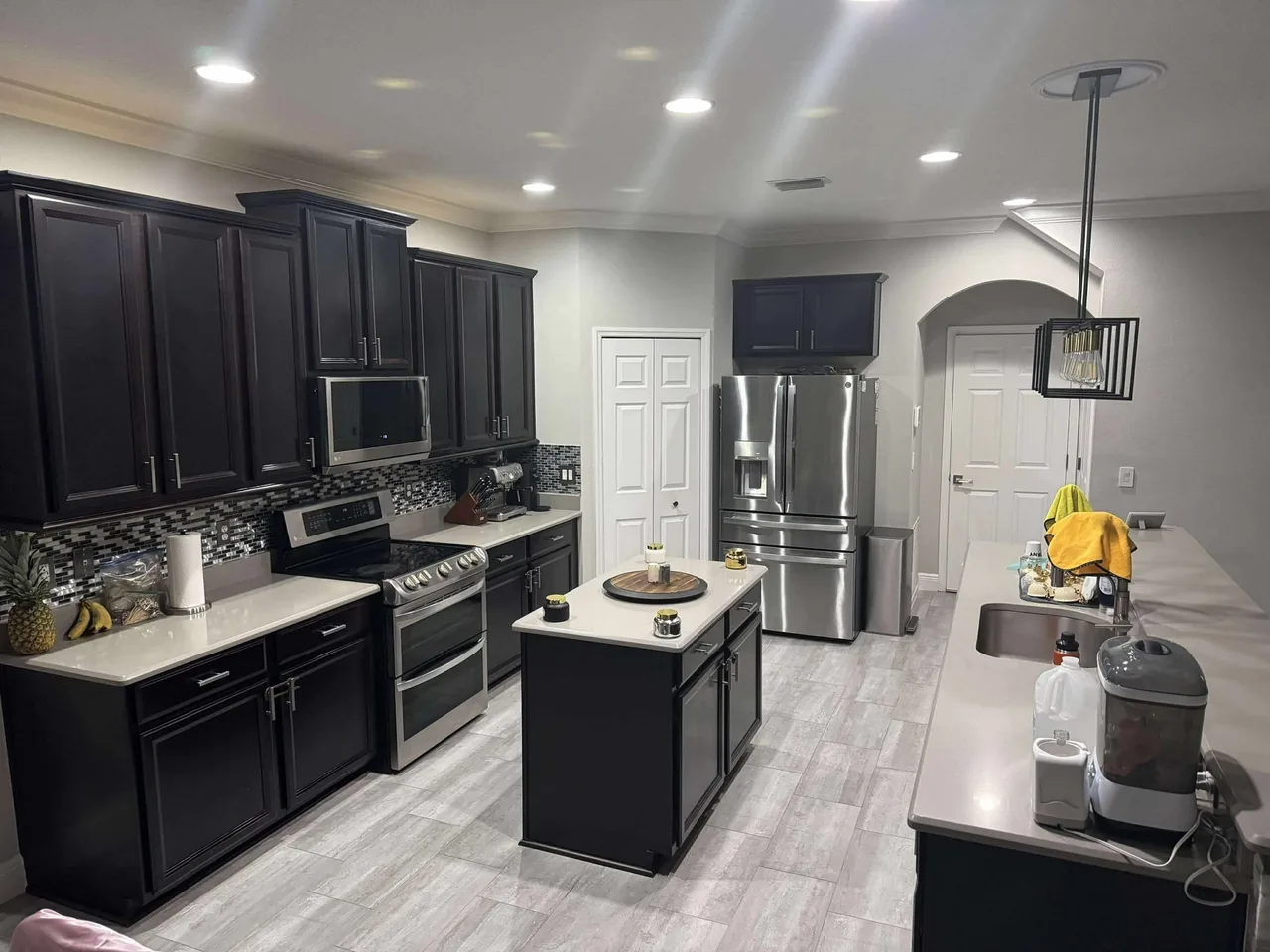 Before: the kitchen with its glass mosaic backsplash, plain light counters and a small island, seen from the living room