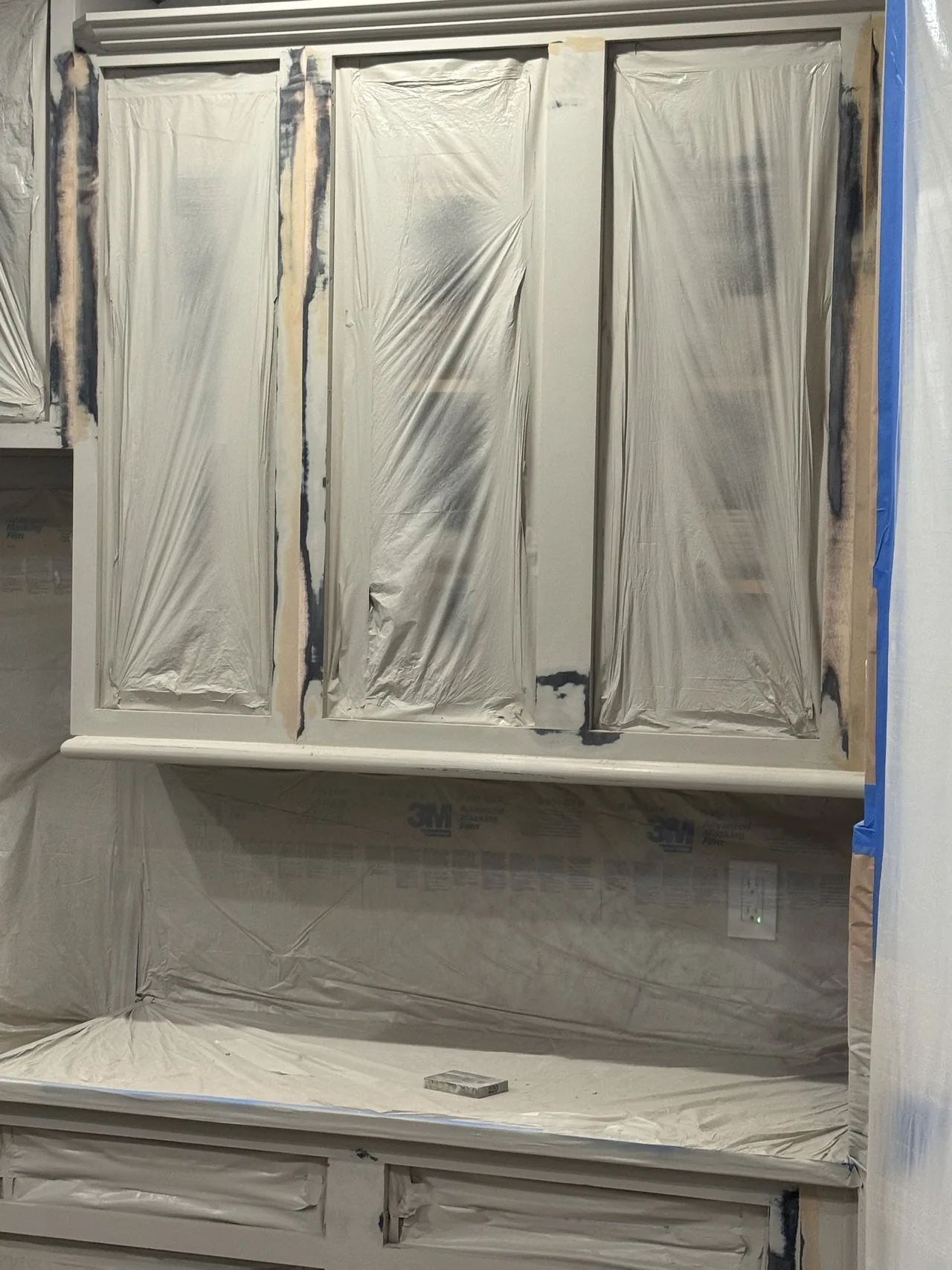 Close-up of masked cabinet doors with the dark original finish showing at the edges under fresh primer