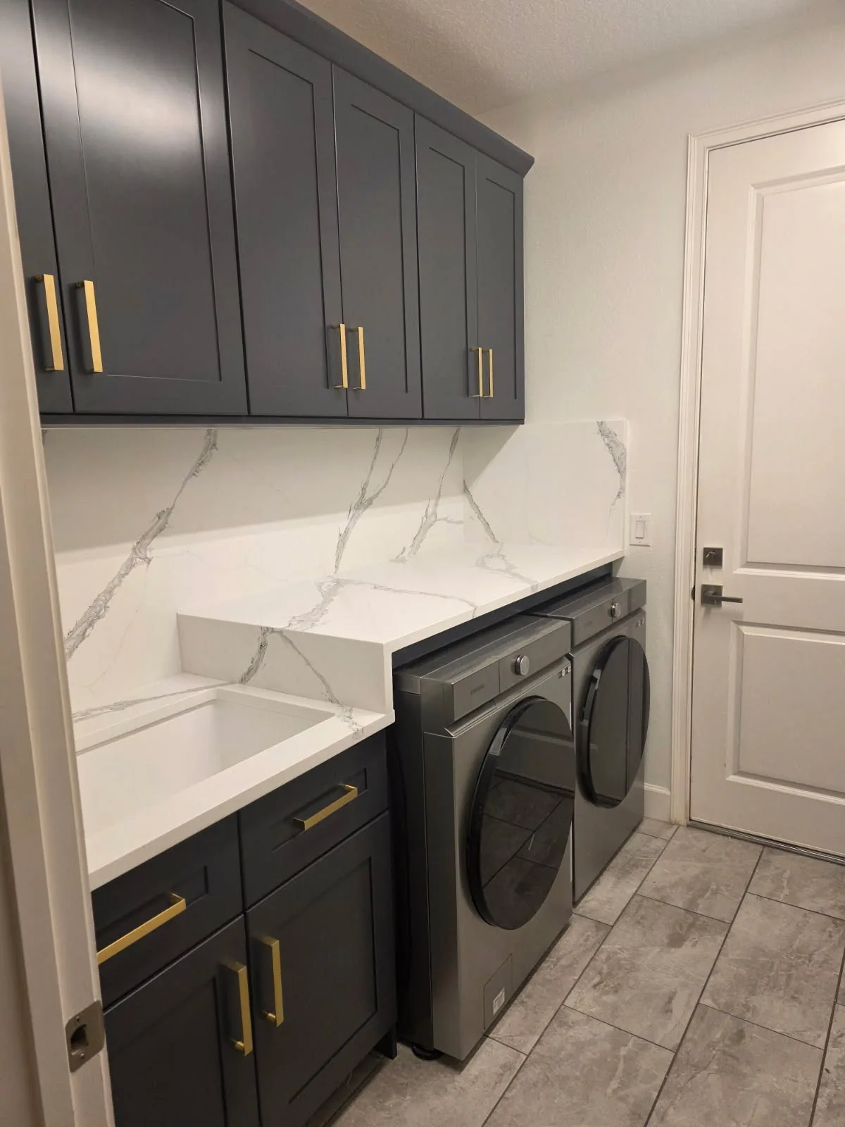 Cuarto de lavado con gabinetes shaker color carbón y cubierta y backsplash de cuarzo