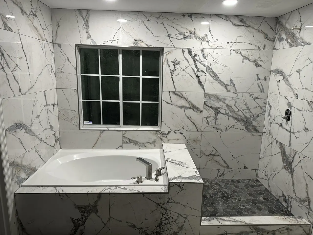 Un baño principal casi terminado, paredes y base de bañera en porcelanato tipo mármol